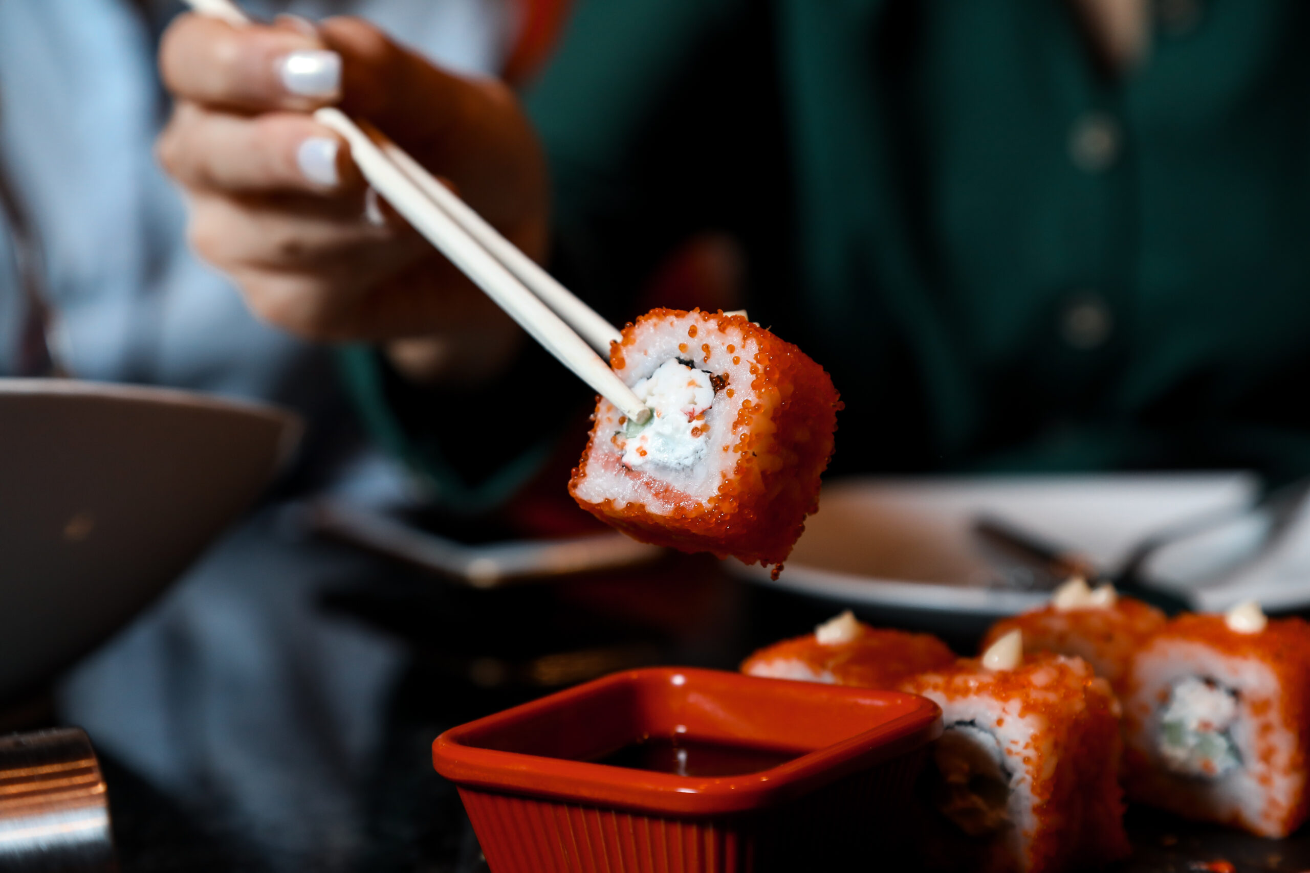 a person dips into a suace sushi rolls while using sticks close-up view