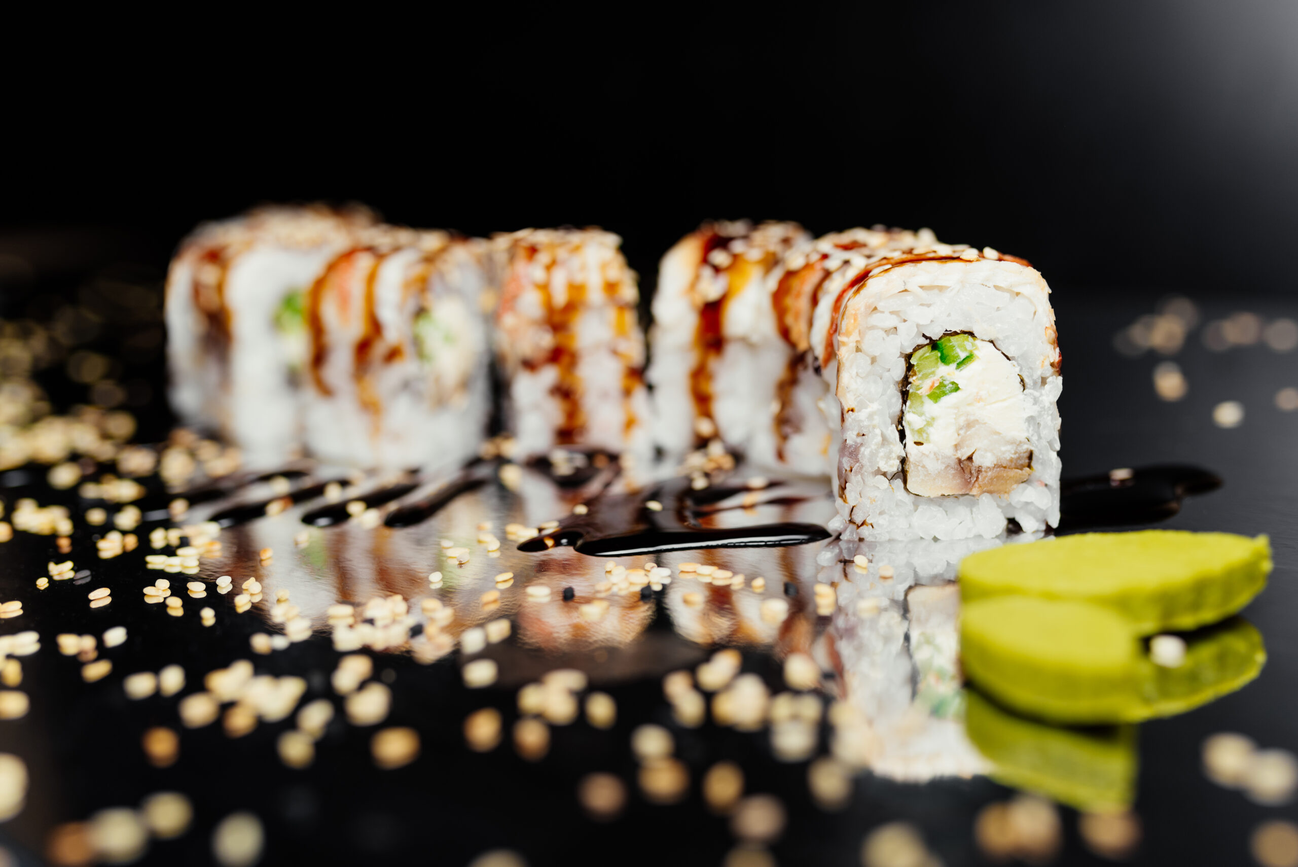 Sushi roll gold dragon on black background made of Nori, Marinated Rice, Cheese, Cucumber, Unangile Whale, Unagi Uguri, Unagi Sauce,Sesame. Sushi menu. Japanese food. Free-space. Close-up.